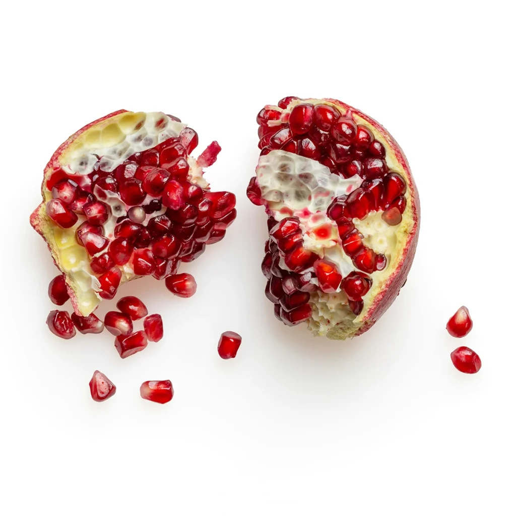 Two halves of a ripe pomegranate with scattered seeds, symbolising nourishment, abundance and vitality in Chandre Prangley's approach to nutrition